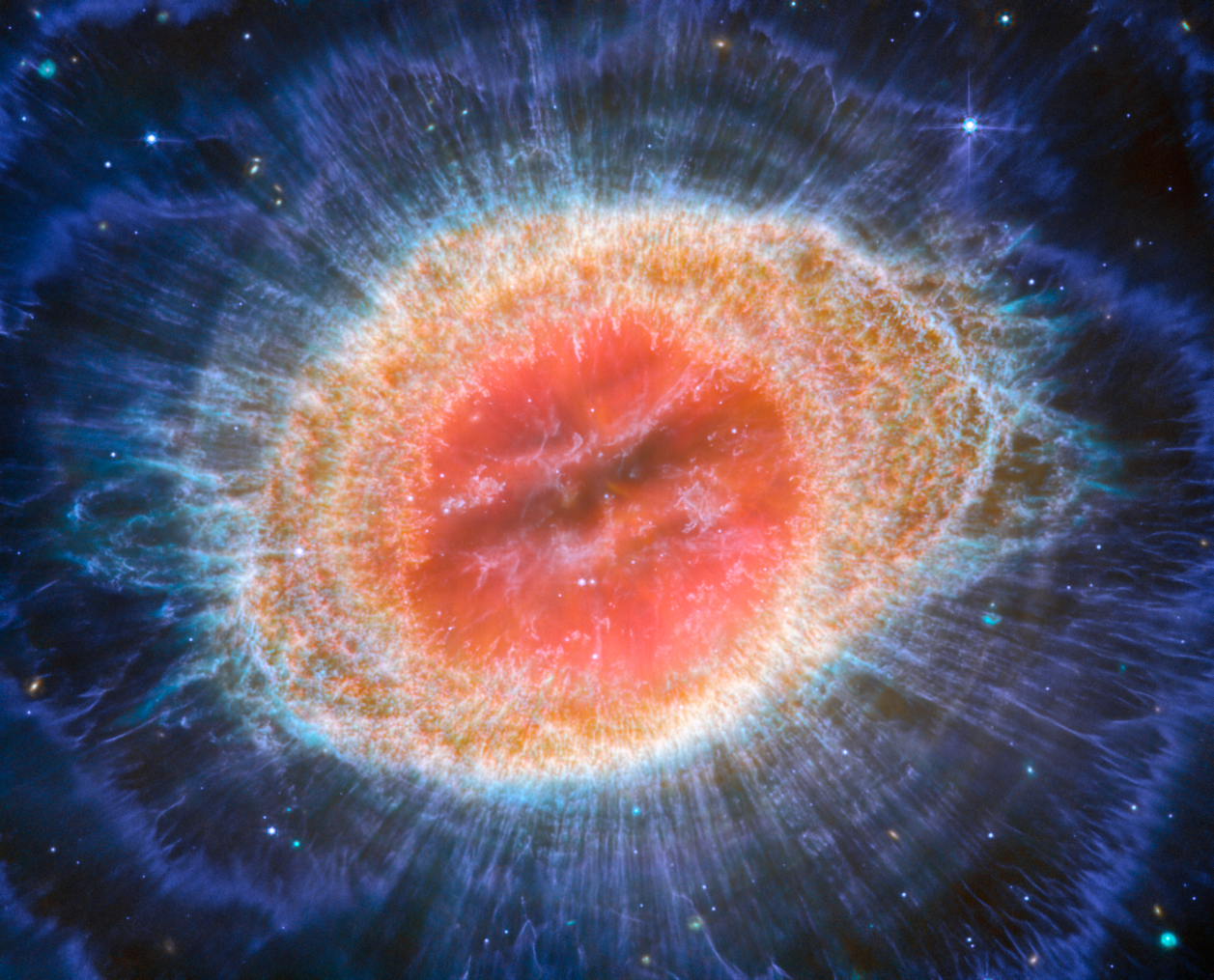 Na ilustracji: Zdjęcie ikonicznej Mgławicy Pierścień (M57, NGC 6720) wykonane przez Teleskop Webba współpracujący z instrumentem MIRI (Mid-InfraRed Instrument). Szczególnie dobrze na tym zdjęciu w średniej podczerwieni uwydatnione są koncentryczne struktury zewnętrznych obszarów pierścienia. Tuż za głównym pierścieniem znajduje się 10 koncentrycznych łuków. Uważa się, że te łuki powstały w wyniku oddziaływania gwiazdy centralnej z małomasywnym gwiezdnym towarzyszem orbitującym w odległości porównywalnej do Ziemia-Pluton w naszym Układzie Słonecznym. Źródło: ESA/Webb, NASA, CSA, M. Barlow (University College London), N. Cox (ACRI-ST), R. Wesson (Cardiff University)