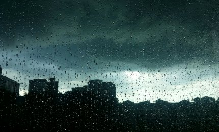 Szyba pokryta kroplami deszczu, przez którą widać panoramę miasta